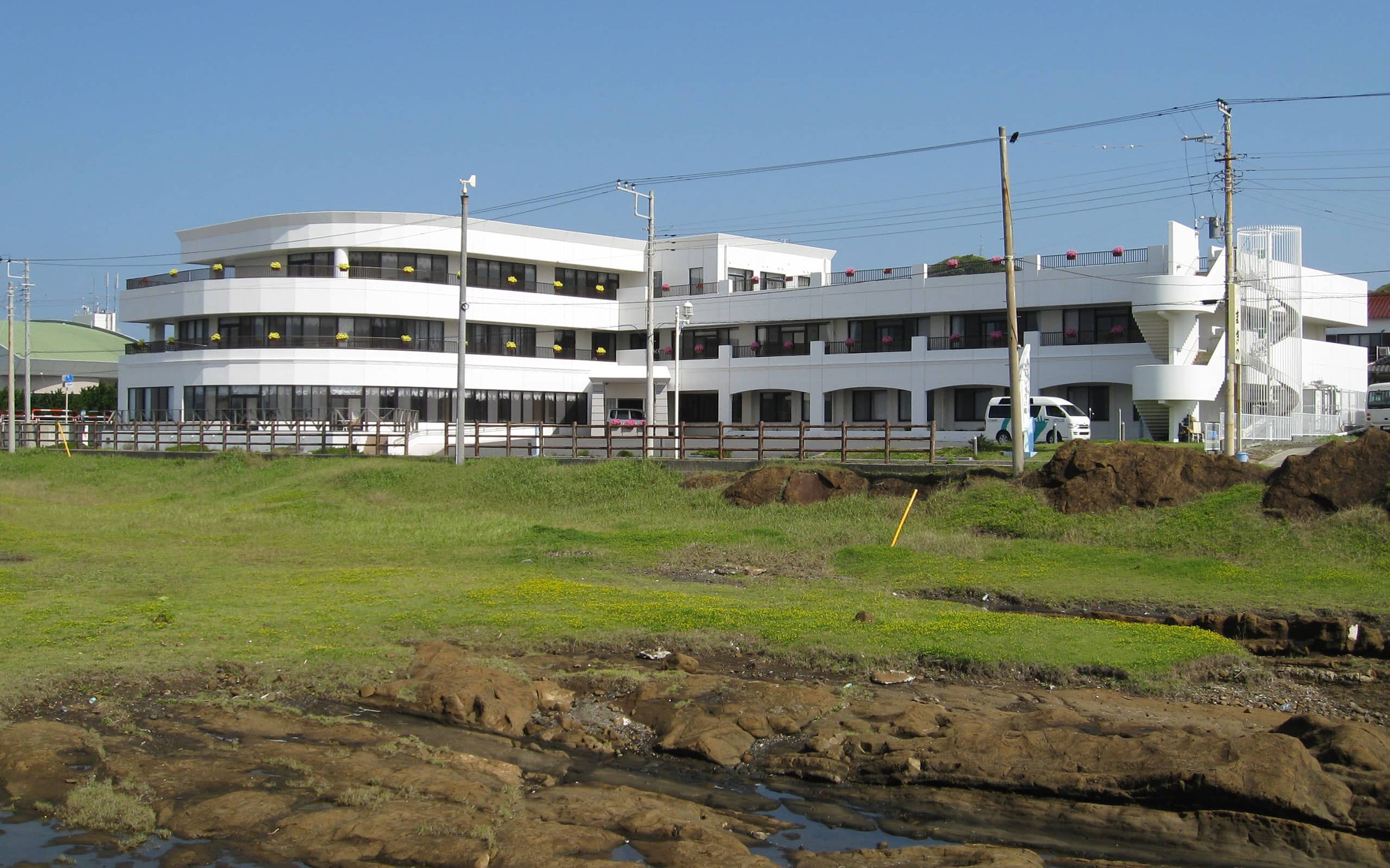 海辺に建つ白い3階建ての介護施設。現代的な建築デザインで、広い敷地が特徴。